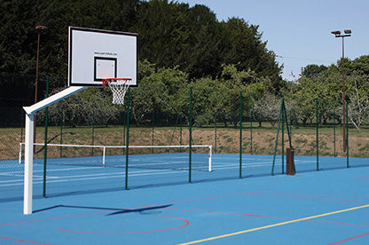 En premier plan, on aperçoit 2 terrains de basket séparés d’un terrain de tennis par un grillage vert.