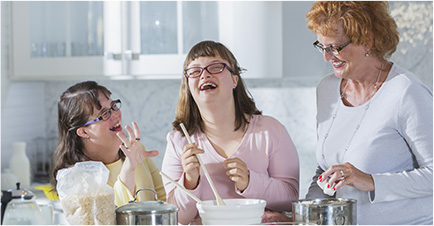3 femmes (2 adolescentes et une adulte) rient aux éclats en préparant une recette de gâteau dans une cuisine.